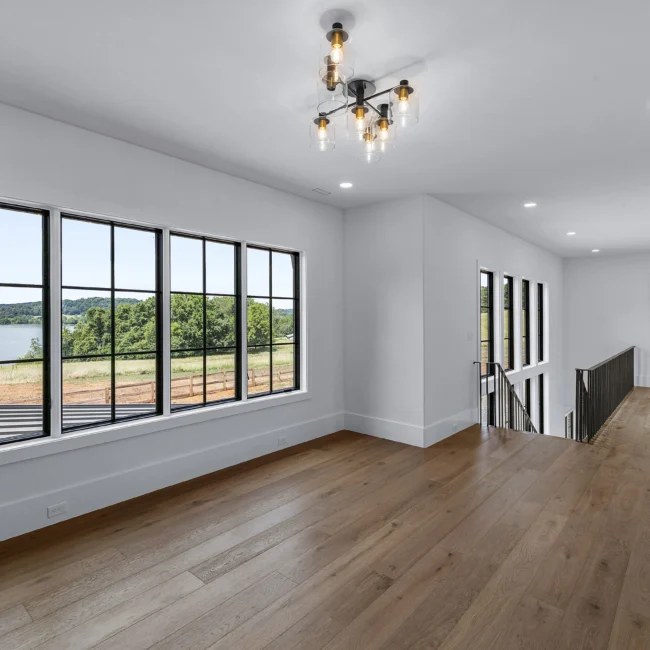 Bedroom with black-framed windows, chandelier and wood floors in Edgewater Estate, a custom home by Mike Stevens Homes