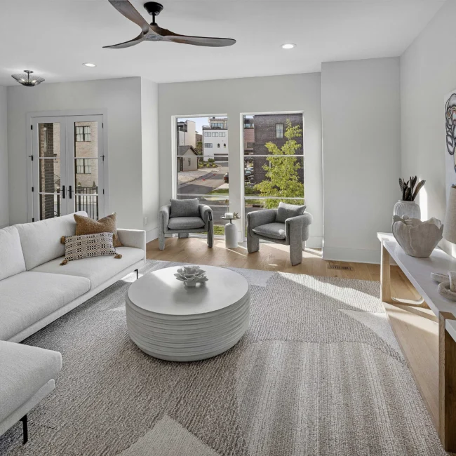 Living room with gray sofa, pillows and sliding glass doors to balcony in The Terrace by Mike Stevens Homes