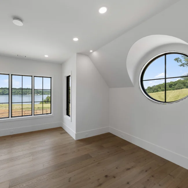 Bedroom with arched round window and wood floors in Edgewater Estate, a custom home by Mike Stevens Homes