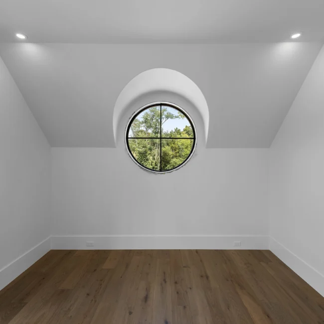 Empty room with round window in gabled wall and wood floors in Edgewater Estate, a custom home by Mike Stevens Homes
