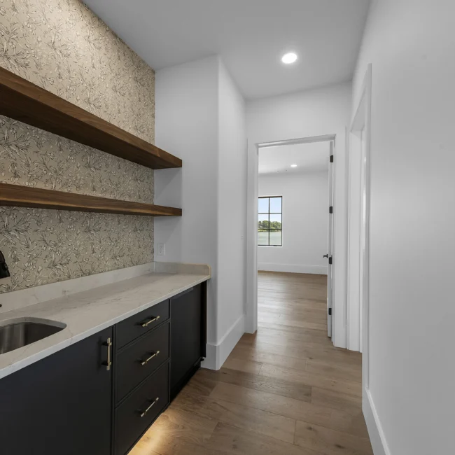 Wet bar with floating walnut shelves and dark cabinets in Edgewater Estate, a custom home by Mike Stevens Homes