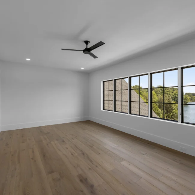 Empty room with ceiling fan and windows overlooking trees in Edgewater Estate, a custom home by Mike Stevens Homes
