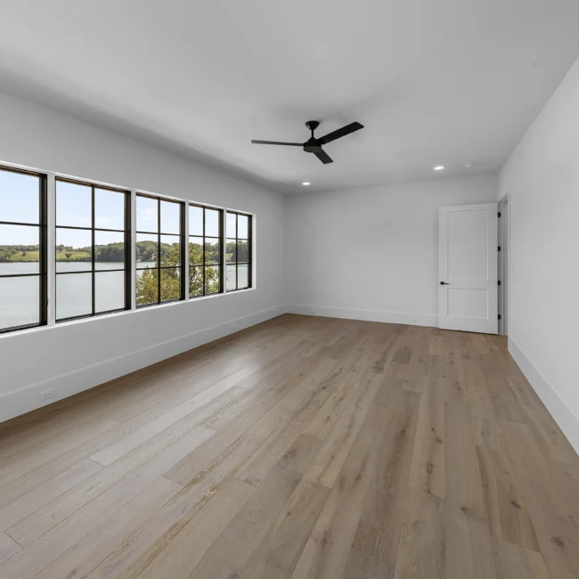 Room with lake-view windows, ceiling fan and wood floors in Edgewater Estate, a custom home by Mike Stevens Homes