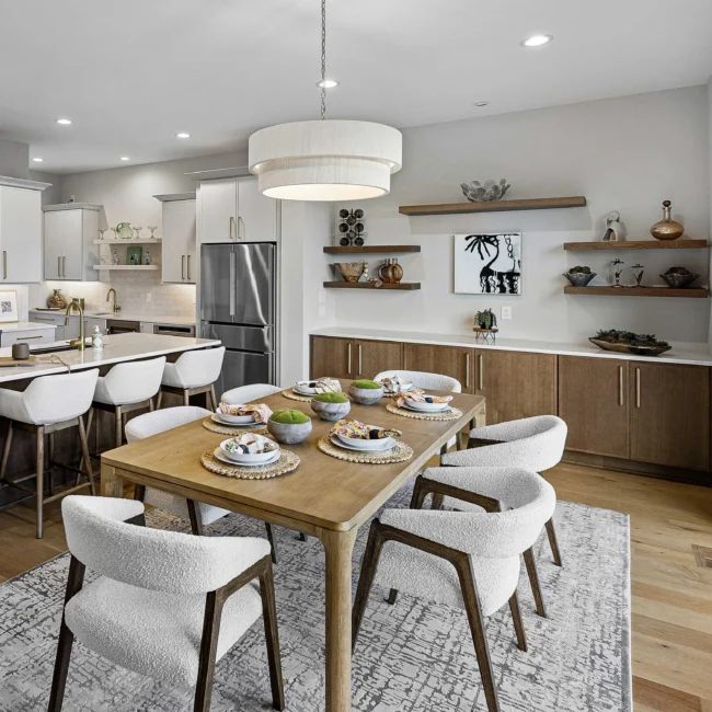 Dining table set for guests beside kitchen with white bar stools in The Terrace by Mike Stevens Homes