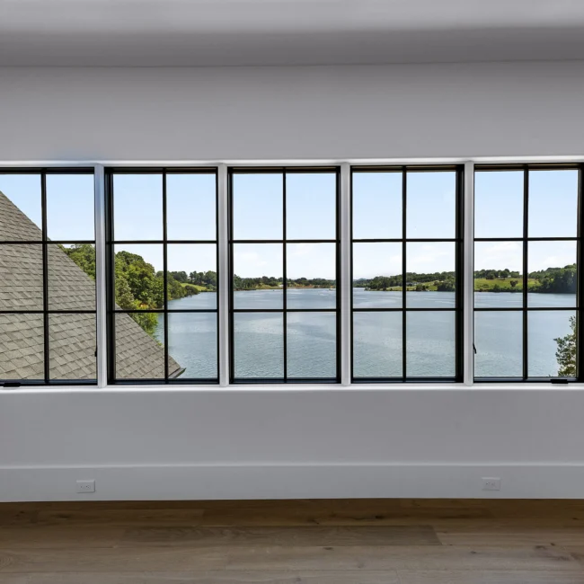 Wall of black-framed windows with lake and wooded view in Edgewater Estate, a custom home by Mike Stevens Homes