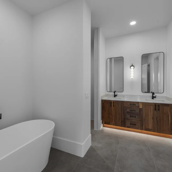 Bath with freestanding tub, twin mirrors and walnut double vanity in Edgewater Estate, a custom home by Mike Stevens Homes