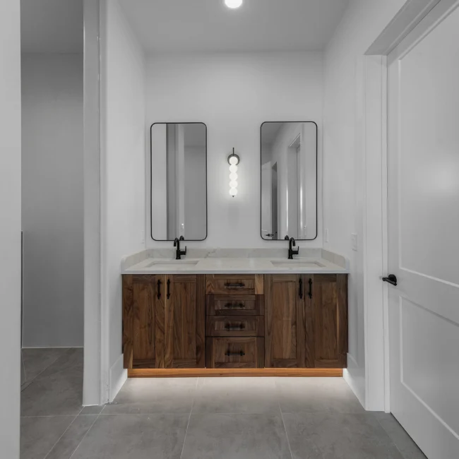 Double vanity with twin mirrors, sconces and walnut cabinets in Edgewater Estate, a custom home by Mike Stevens Homes
