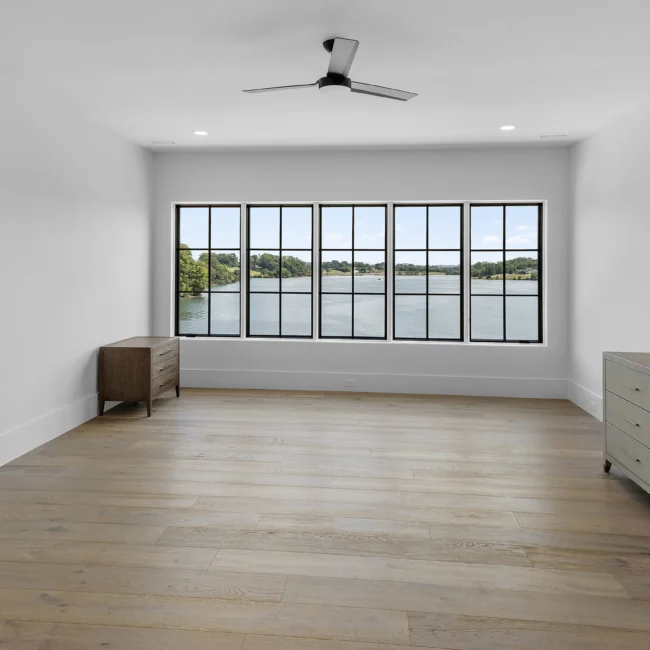 Bedroom with five-pane lake-view windows and ceiling fan in Edgewater Estate, a custom home by Mike Stevens Homes