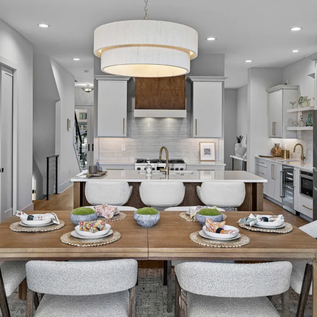 Kitchen and dining area with drum pendant and white upholstered chairs in The Terrace by Mike Stevens Homes