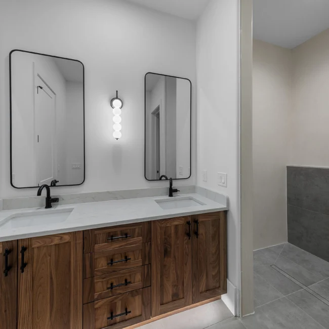 Double vanity with walnut cabinets, sconce mirrors and gray tile in Edgewater Estate, a custom home by Mike Stevens Homes