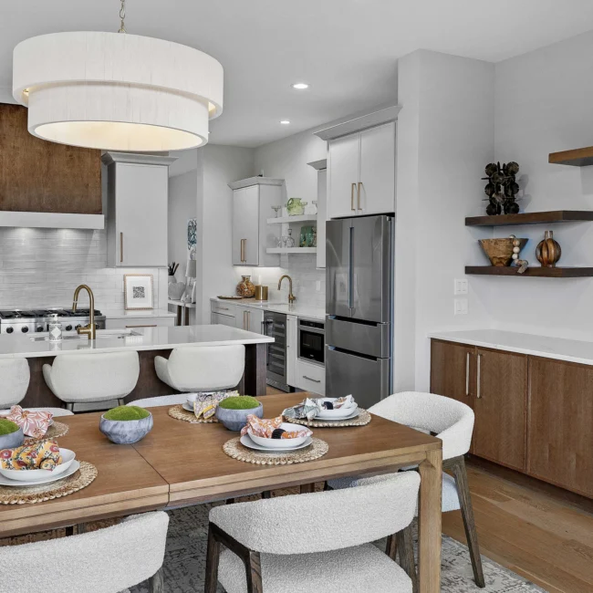Kitchen with range hood, white cabinets and wood dining table in The Terrace by Mike Stevens Homes