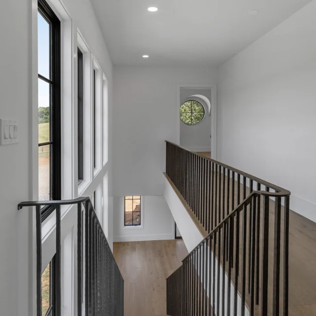 Upper landing with black iron railing and round window in Edgewater Estate, a custom home by Mike Stevens Homes
