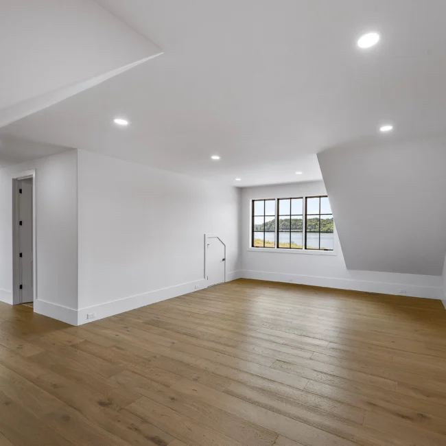 Empty bonus room with sloped ceiling and lake-view window in Edgewater Estate, a custom home by Mike Stevens Homes