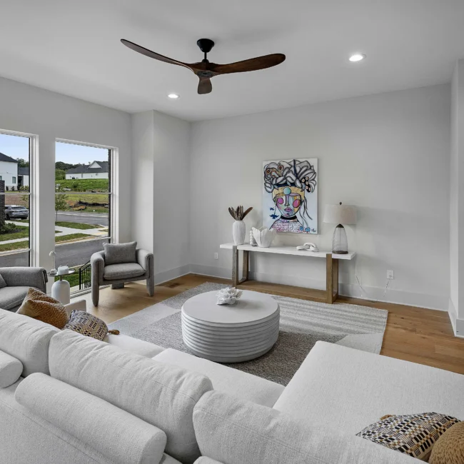 Living room with white sofa, ceiling fan and bright windows in The Terrace by Mike Stevens Homes