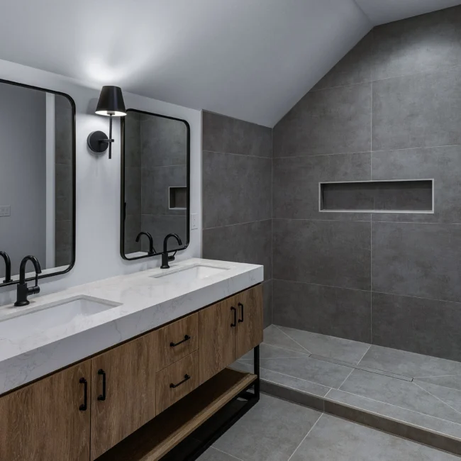 Primary bath with dual mirrors, gray walk-in shower and wood vanity in Edgewater Estate, a custom home by Mike Stevens Homes