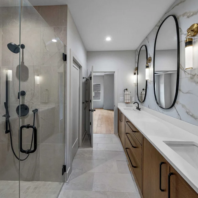 Bathroom with walk-in glass shower and dual round mirrors in The Terrace by Mike Stevens Homes