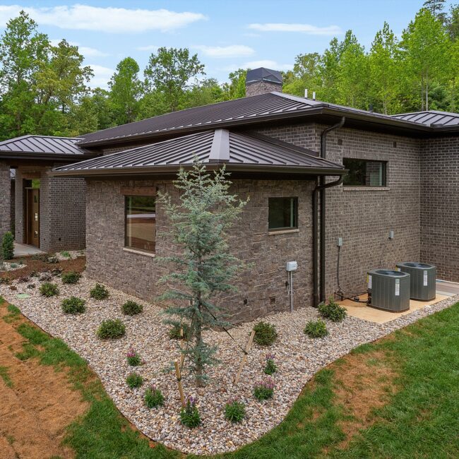 Dark brick and stone exterior with bronze standing-seam hip roofs at Modern Prairie by Mike Stevens Homes