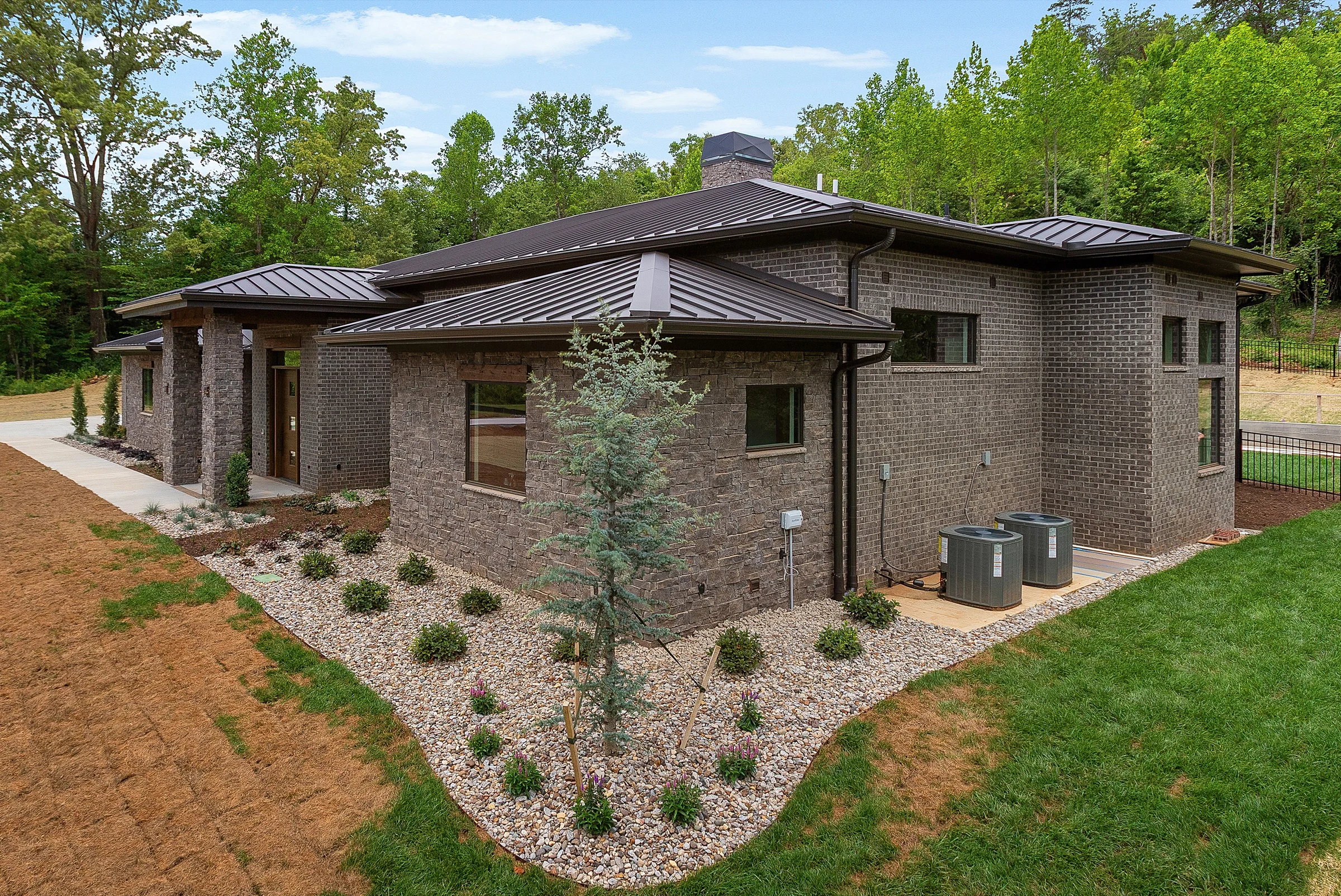 Dark brick and stone exterior with bronze standing-seam hip roofs at Modern Prairie by Mike Stevens Homes
