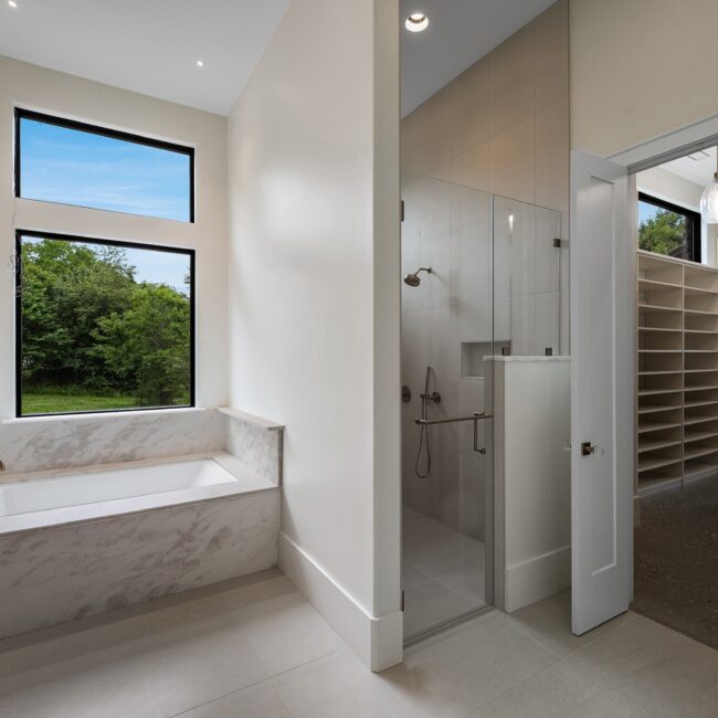 Marble-wrapped soaking tub under a tall black window in Modern Prairie by Mike Stevens Homes