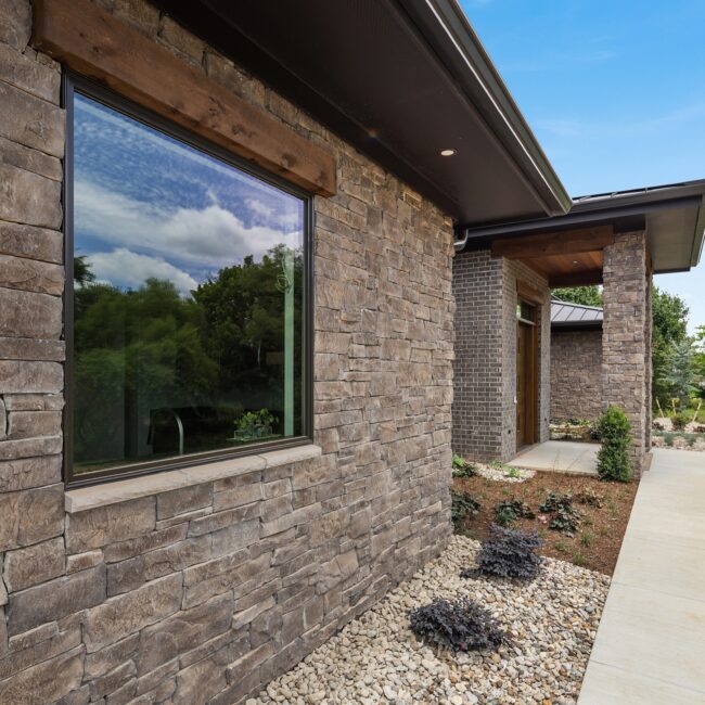 Stacked stone wall under a deep bronze roof overhang at Modern Prairie, a custom home by Mike Stevens Homes