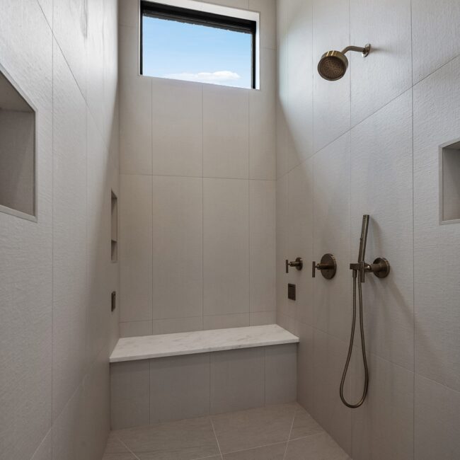 Walk-in shower with large-format tile, bench and niches in Modern Prairie by Mike Stevens Homes
