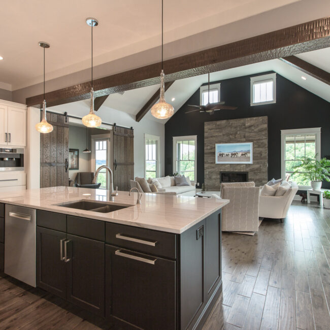 Vaulted great room with dark beams and stone fireplace wall in Rockport Gray Farmhouse by Mike Stevens Homes