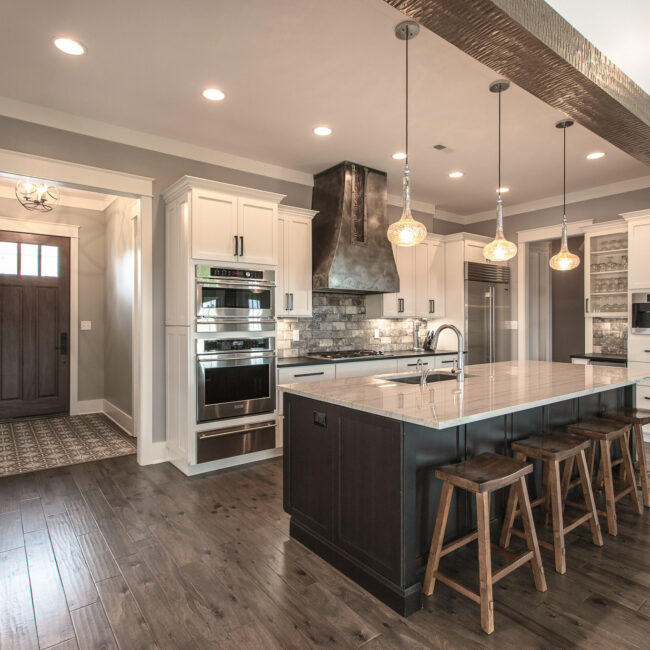 Open kitchen with beamed ceiling and view to the front door in Rockport Gray Farmhouse by Mike Stevens Homes