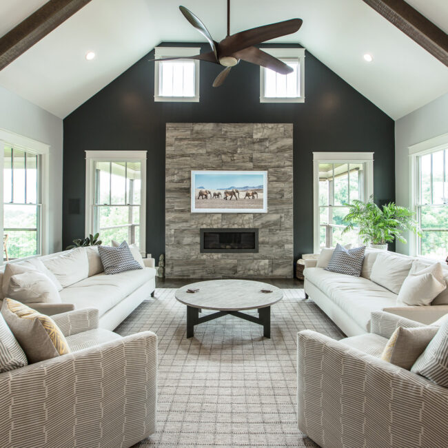 Living room with stone-clad fireplace on a charcoal accent wall in Rockport Gray Farmhouse by Mike Stevens Homes