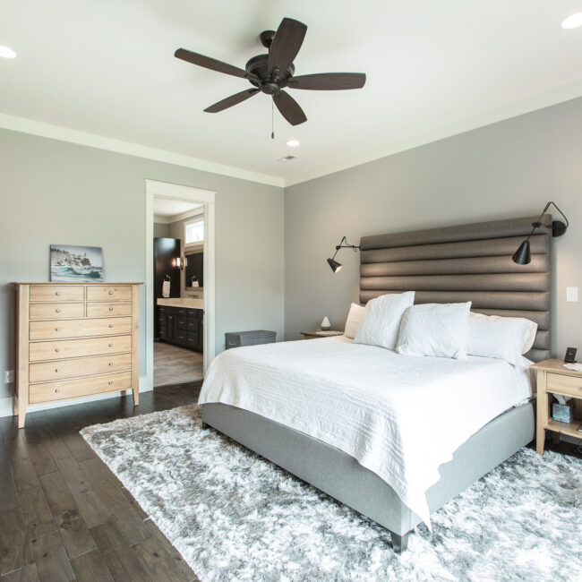 Primary bedroom with upholstered headboard wall in Rockport Gray Farmhouse by Mike Stevens Homes