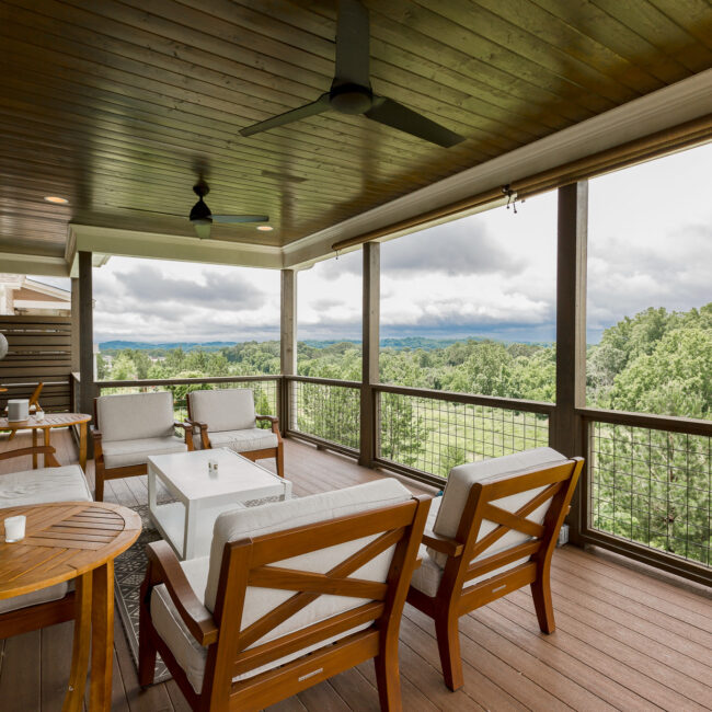 Upper covered porch with wood-plank ceiling and hillside views at Rockport Gray Farmhouse by Mike Stevens Homes