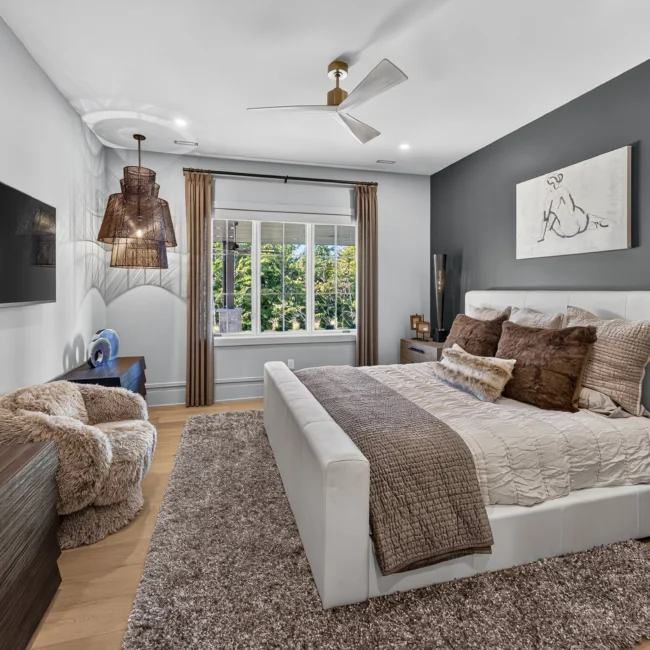 Bedroom with a charcoal accent wall, upholstered white bed, shag rug, wall-mounted TV and a woven pendant light by the window