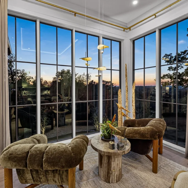 Breakfast nook at dusk with green tufted chairs, a round table and tall black-framed windows with drapes