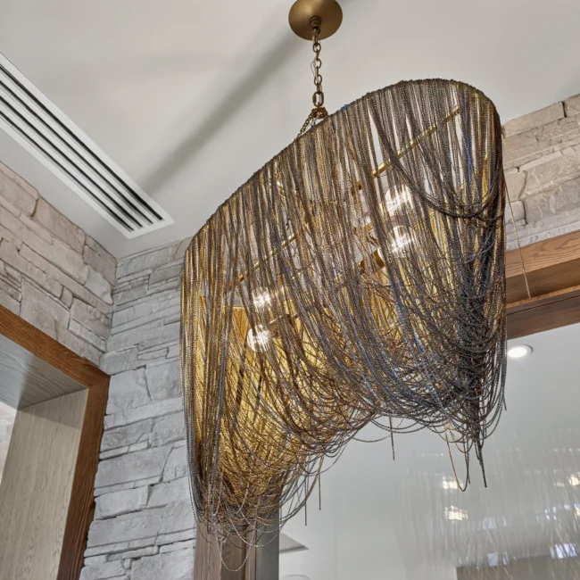 Brass chain-fringe chandelier hanging beside a stacked stone wall and a wood-trimmed doorway