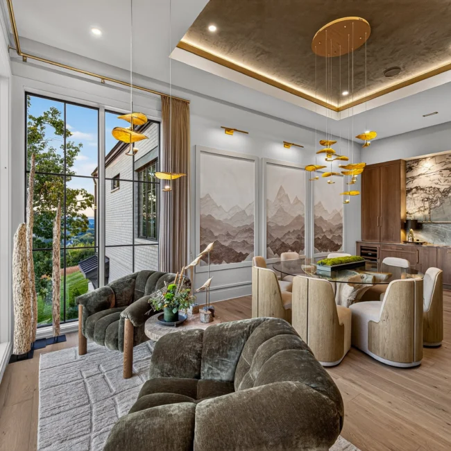 Dining room with a gold disc light fixture, a round table, mountain murals and olive green velvet chairs by a tall window
