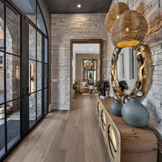 Entry hall by Mike Stevens Homes with a stone wall, brass round mirror over a carved wood console and arched glass doors