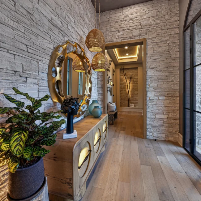 Entry hall with a stacked stone wall, a gold mirror over a console, woven pendants and glass doors on the right