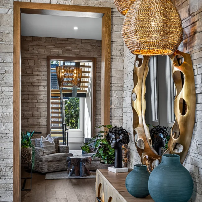 Sunset Heights gold cutout mirror and woven pendants against stacked stone, with a sitting area visible down the hall