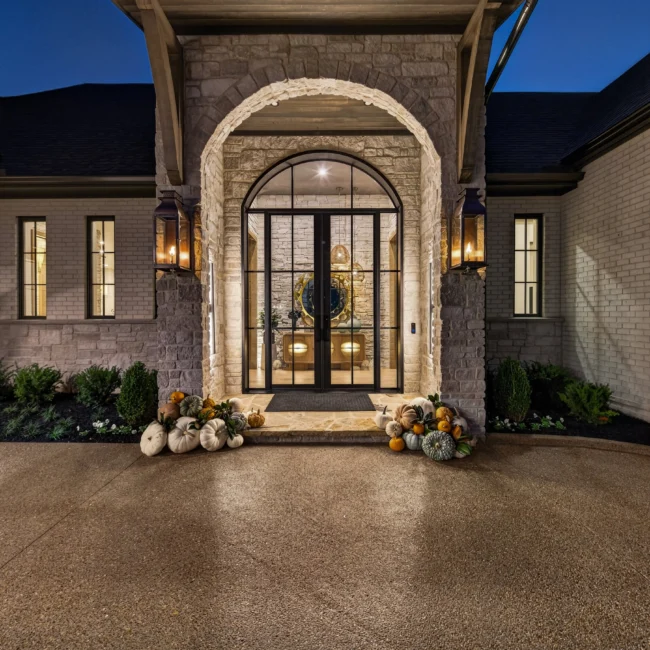 Illuminated arched front door with black steel and glass, brass lanterns and pumpkins, under a dark night sky