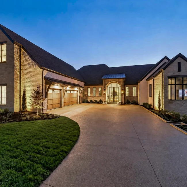 Sunset Heights front exterior at dusk with lit windows, a brick and stone facade, a three-bay garage and a curving drive
