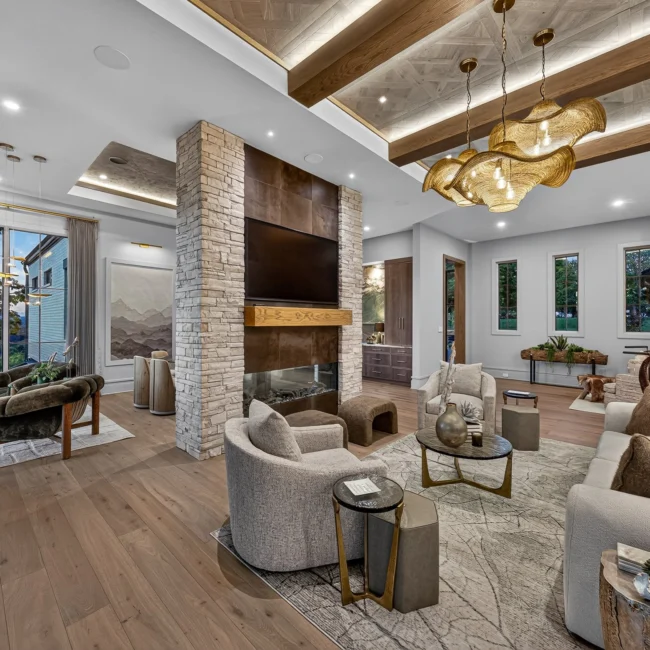 Sunset Heights great room with a beamed parquet ceiling, stone fireplace with TV, cream armchairs, a velvet sofa and tall windows