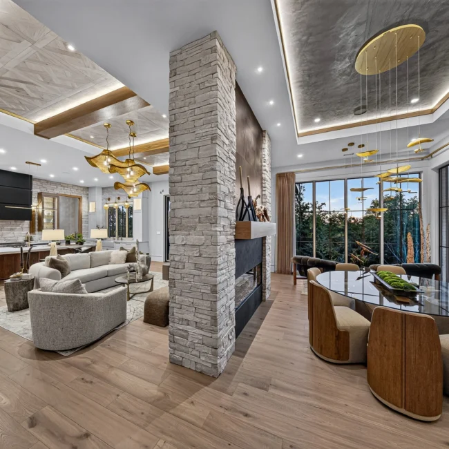 Great room and dining area seen across a stone column, with a beamed ceiling, sofas and a plaster tray ceiling