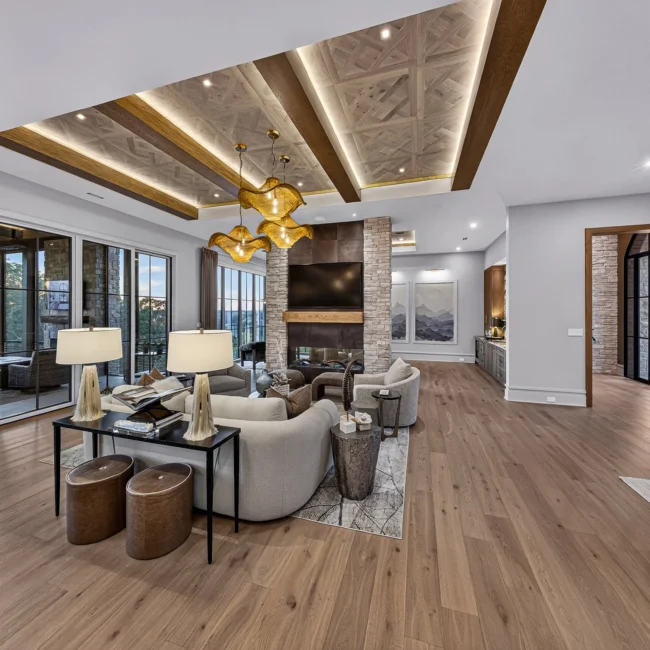 Sunset Heights great room with sofas by sliding glass doors, wood beams across a parquet ceiling and a stone fireplace column