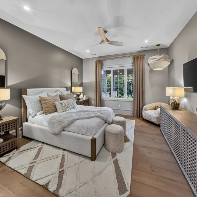 Wide view of the guest bedroom with a white upholstered bed, wood slat dresser, wall TV and arched mirror