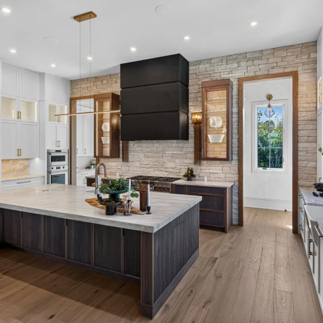 Kitchen by Mike Stevens Homes with a stone-topped island, black range hood over stacked stone and white paneled cabinets