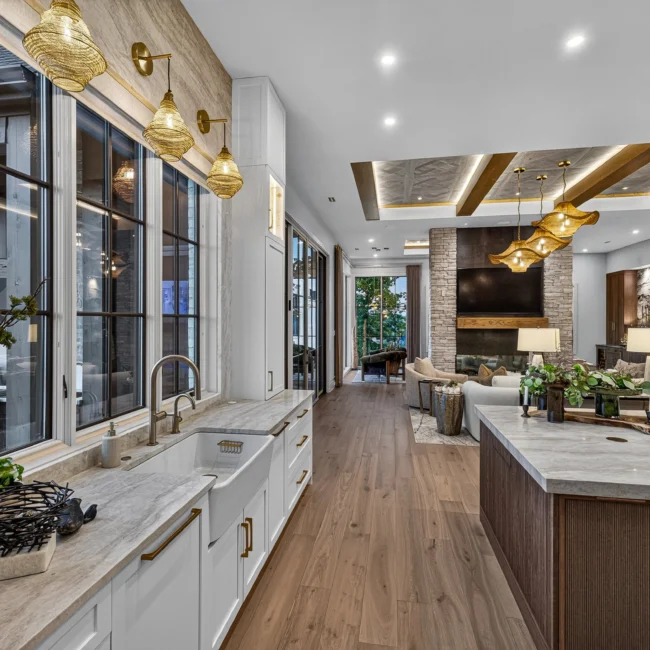 Sunset Heights kitchen sink counter in the foreground with brass sconces, tall windows and the island and great room beyond