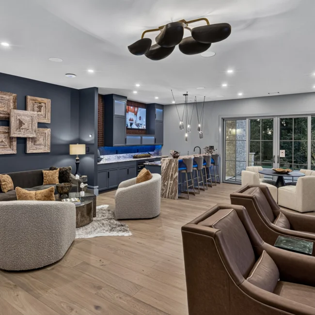 Lower-level lounge with a black ceiling light fixture, a navy accent wall, leather chairs and a bar with stools