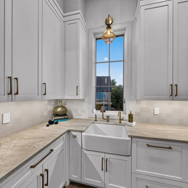 Pantry corner with a white farmhouse sink, brass faucet, a small window and a brass pendant over a stone counter