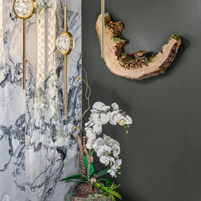 Powder room detail with a veined marble wall, round brass sconces, a live-edge wood ornament and orchids on the vanity