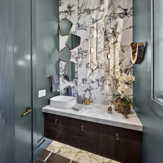 Powder room with a teal-gray wall, white vessel sink on a dark wood vanity, veined marble feature wall and patterned stone floor