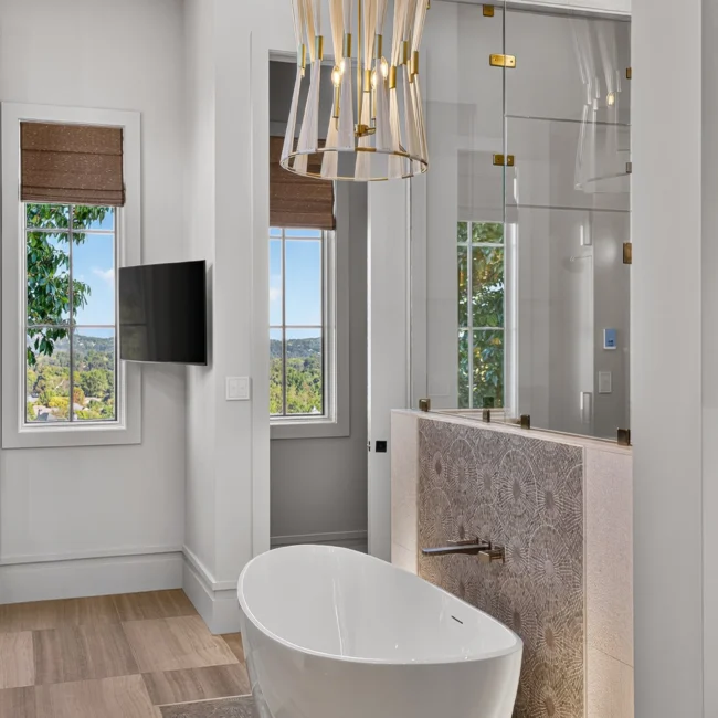Sunset Heights primary bath with a freestanding white tub, a glass-walled shower and a brass-banded pendant light beside a window